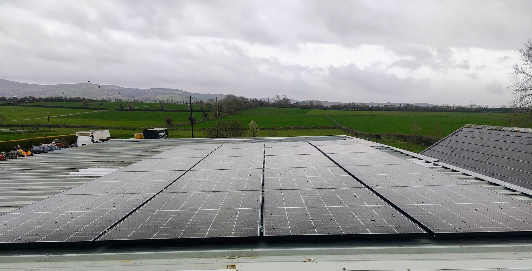 Solar panels on the roof of a farm building, with fields and hills behind
