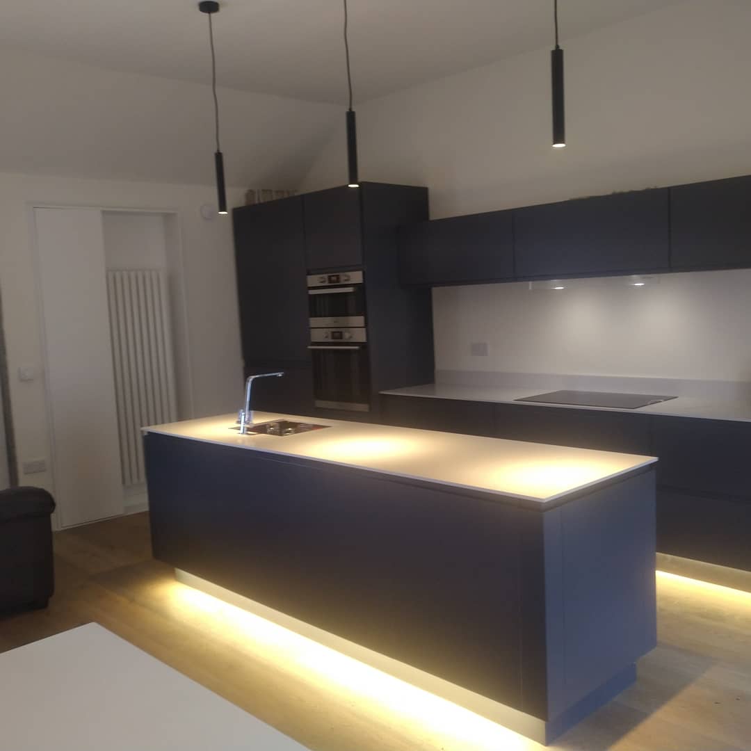 A kitchen island with pendant lights above and lighting under the plinth